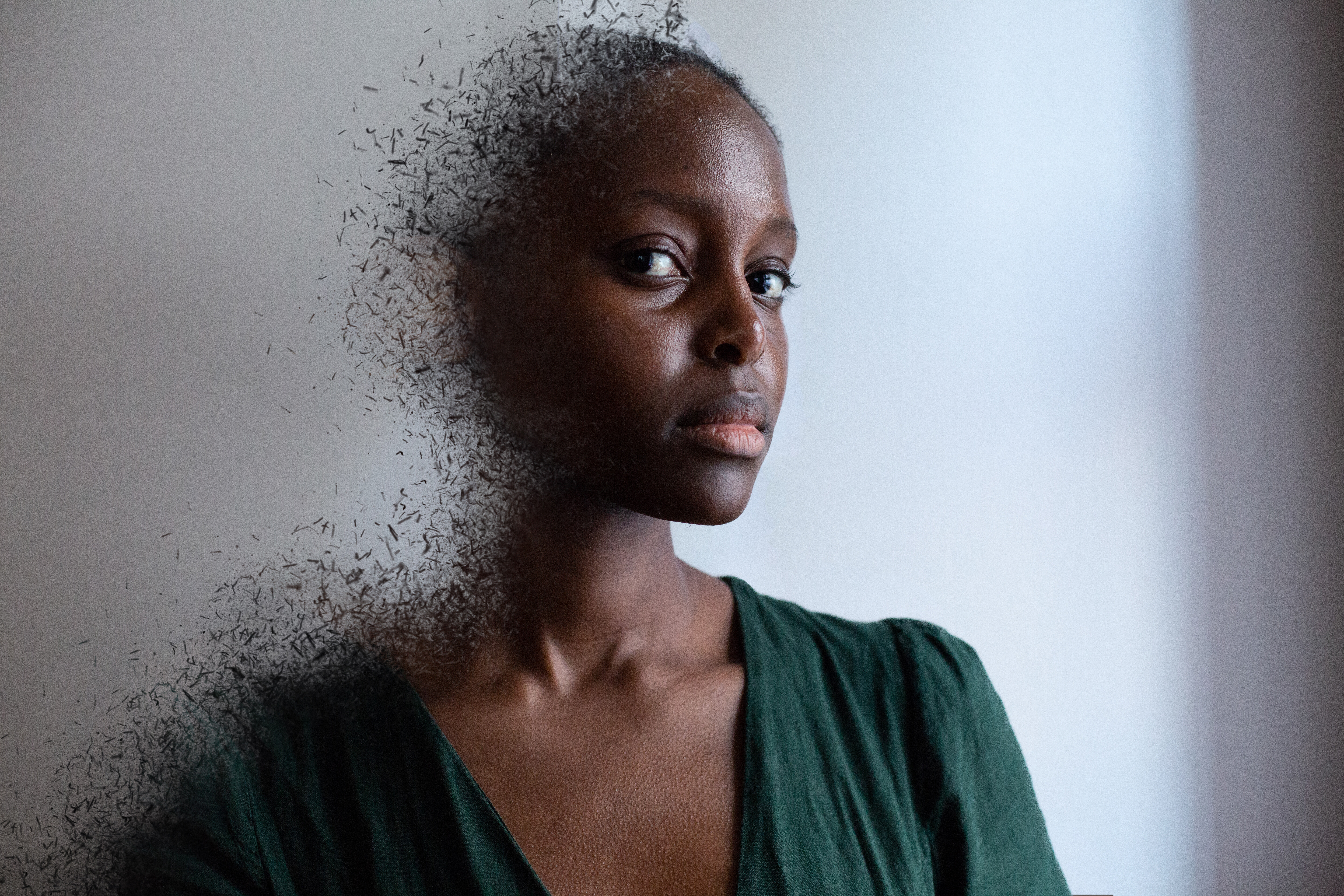 This picture is a close-up photo of a woman, looking into the camera. With the help of photo editing, it looks like the left side of her torso is detaching and scattering in tiny little pieces in all directions.