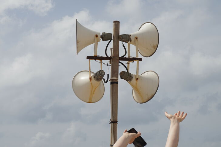 Four loudspeakers pointing in different directions. There are also two arms protruding into the picture, one of which is carrying a cell phone.