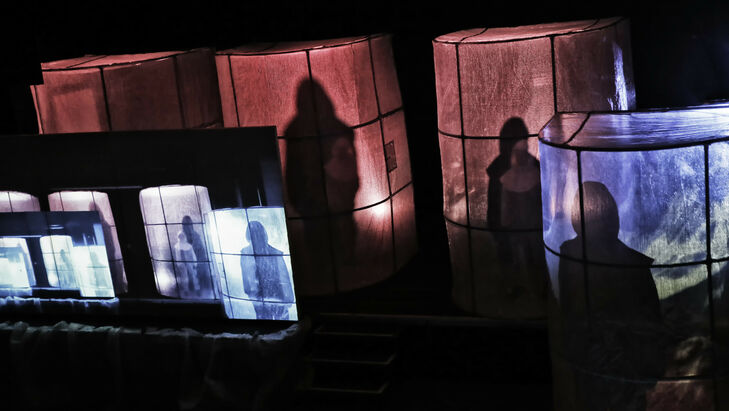 Three large, red-lit light boxes made of fabric, in which there are people of whom you can only see the shadows.